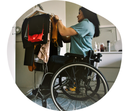Une femme en fauteuil roulant choisit des vêtements dans un dressing adapté dont la tringle est prévue pour s'abaisser afin de faciliter l'accessibilité.